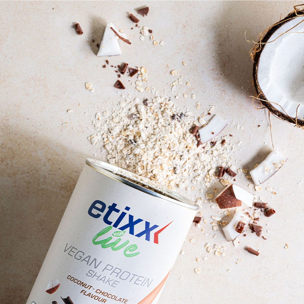 Open blik etixx Live Vegan Protein Shake. Kokos- en chocoladestukjes verspreid. Halve kokosnoot op de achtergrond.
