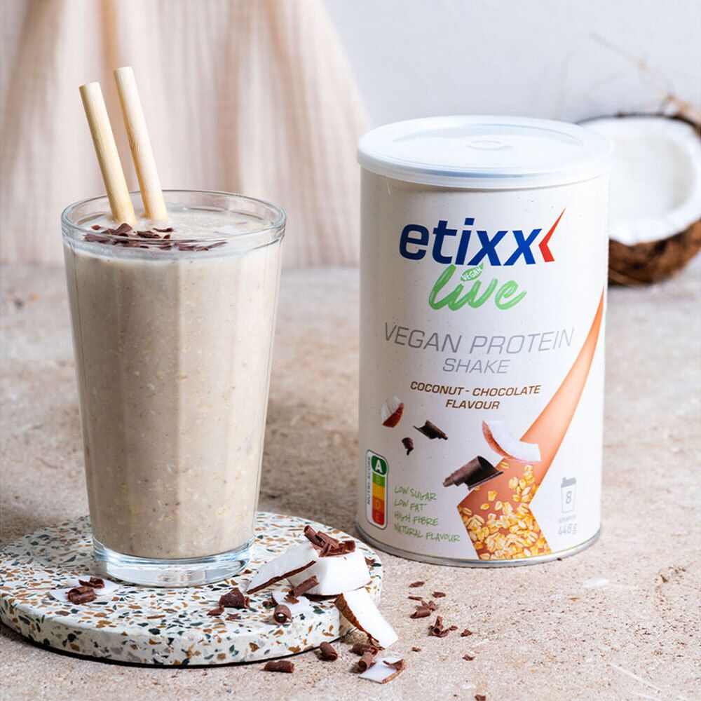 Glas etixx Live Vegan Protein Shake. Kokos- en chocoladesnippers. Blik ernaast. Rietjes. Halve kokosnoot.