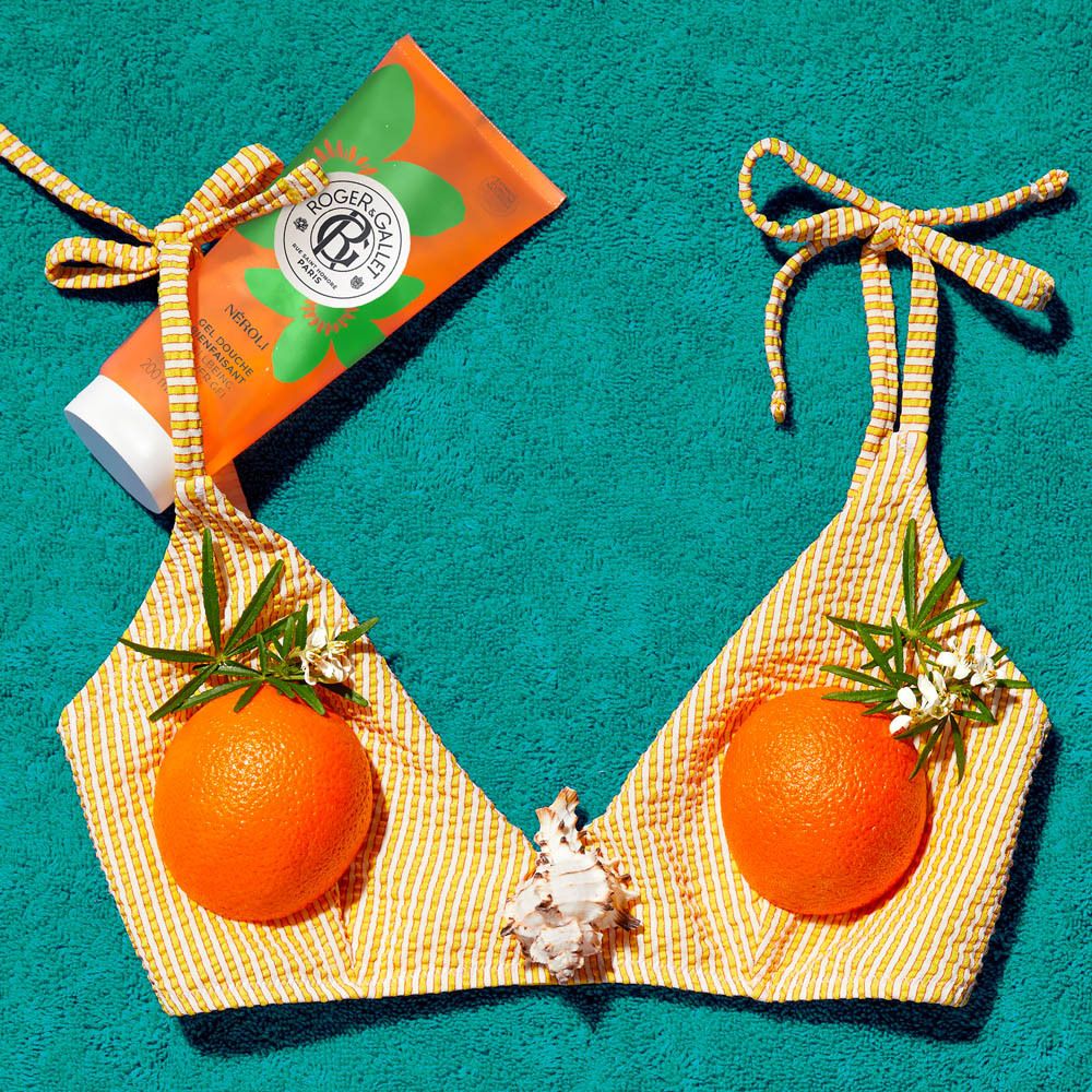 Gel douche NÉROLI avec bikini jaune, oranges et coquillage. Arrangement de plage.