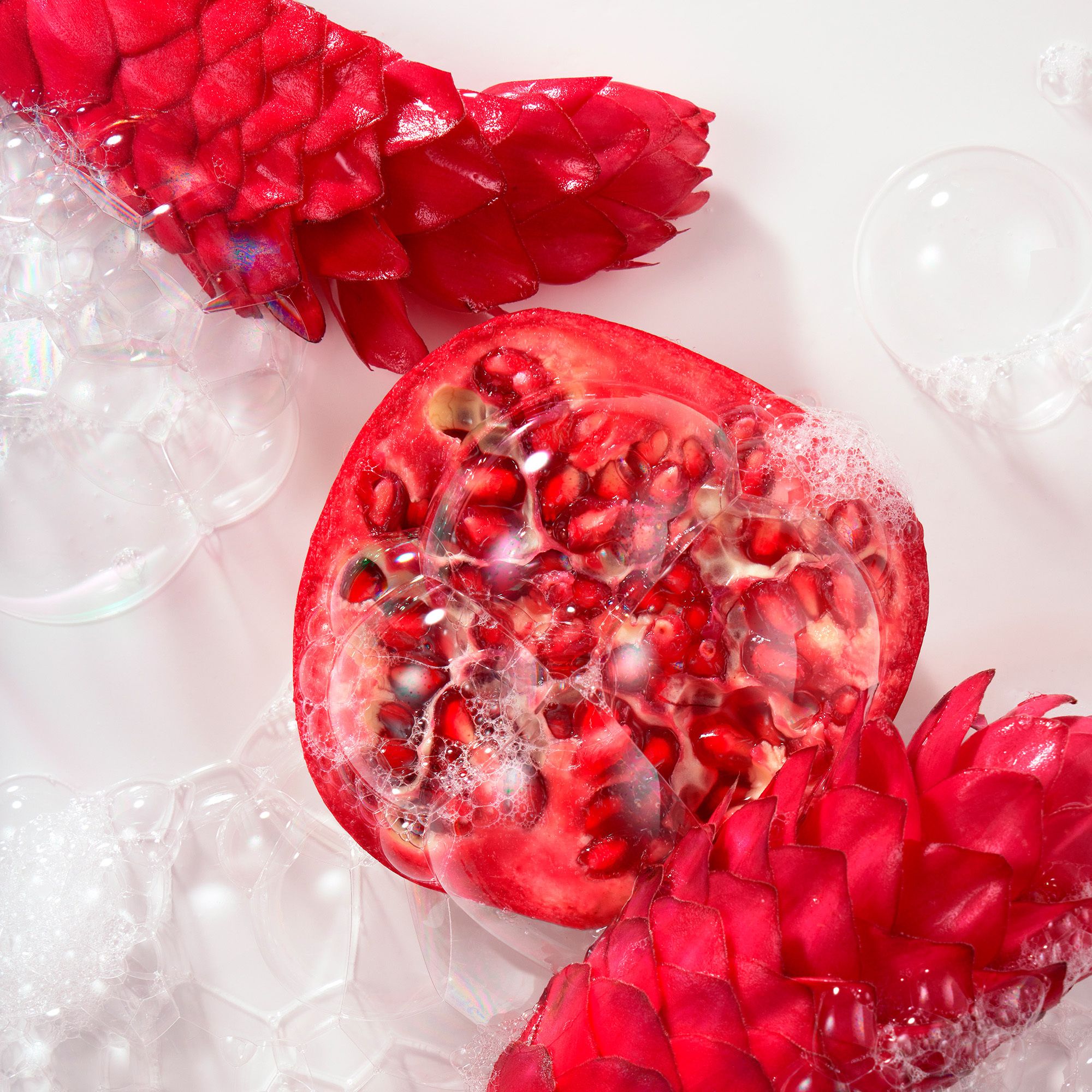 Halve granaatappel met bellen en rode bloemen op witte achtergrond.