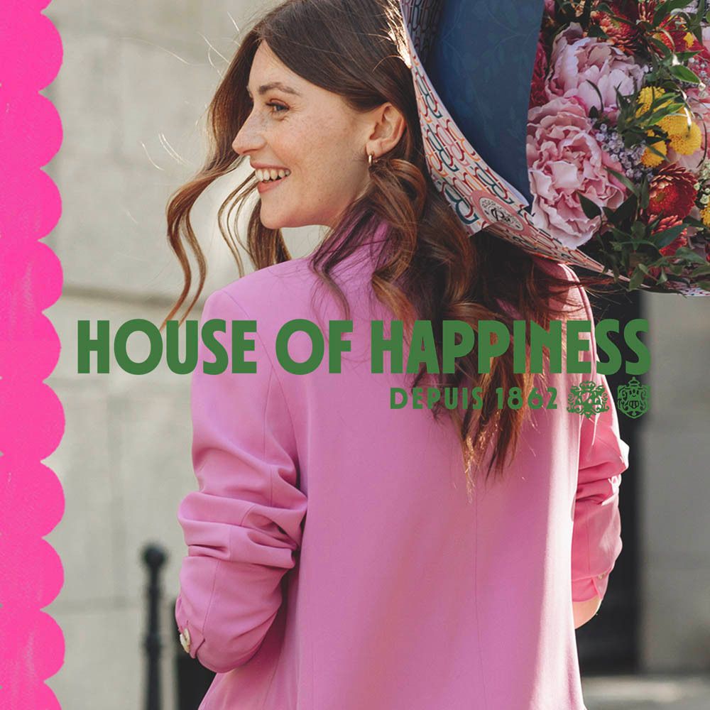 Vrouw in roze jas, boeket bloemen. Tekst: House of Happiness, Depuis 1862.
