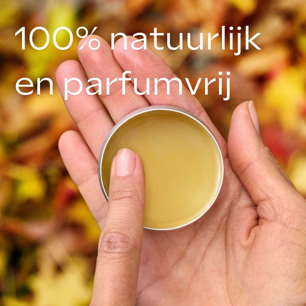 Handen houden een open potje balsem vast. Tekst: 100% natuurlijk en parfumvrij. Achtergrond: herfstbladeren.