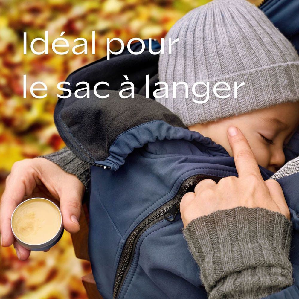 Enfant en combinaison bleue, bonnet. Une main touche le visage de l'enfant. Pot de baume. Idéal pour le sac à langer.