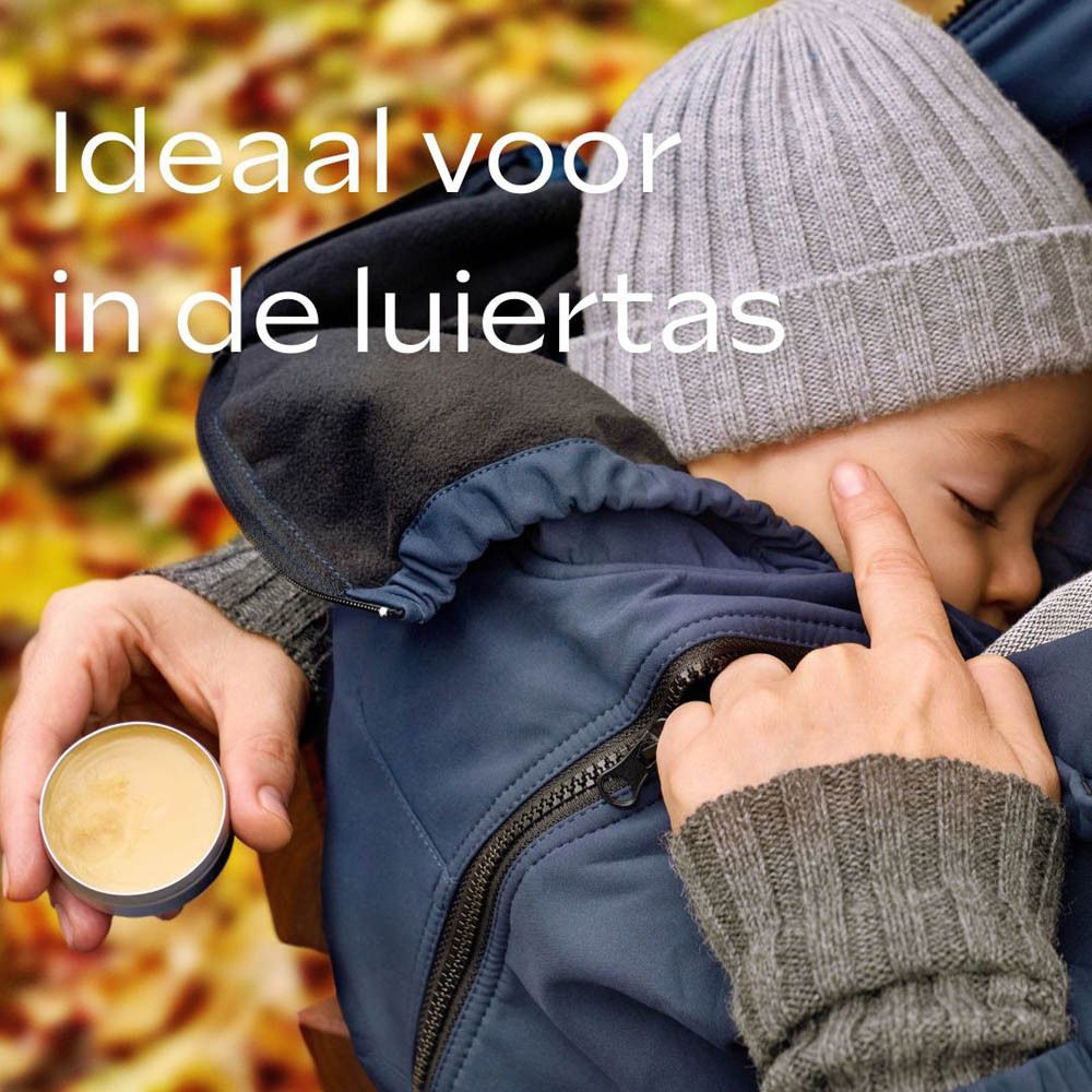 Kind in blauw pak, muts. Een hand raakt het gezicht van het kind aan. Potje balsem. Ideaal voor in de luiertas.