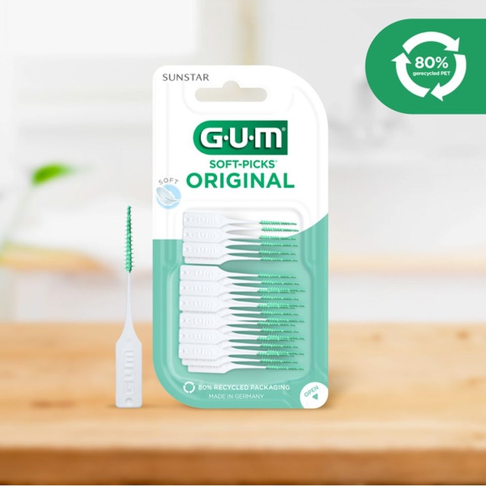 Verpakking GUM Soft-Picks Original. Groen-witte picks. 80% gerecycled PET. Op een houten tafel.