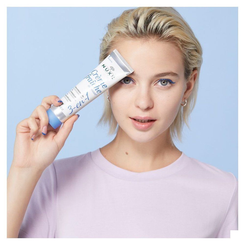 Vrouw houdt een Nuxe Crème fraîche de beauté tube voor haar gezicht.