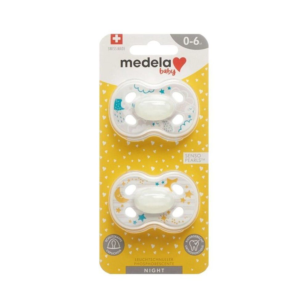 Deux sucettes Medela Baby sur emballage jaune. Motifs étoiles et lune. Recommandé pour les 0-6 mois. Tétines phosphorescentes.