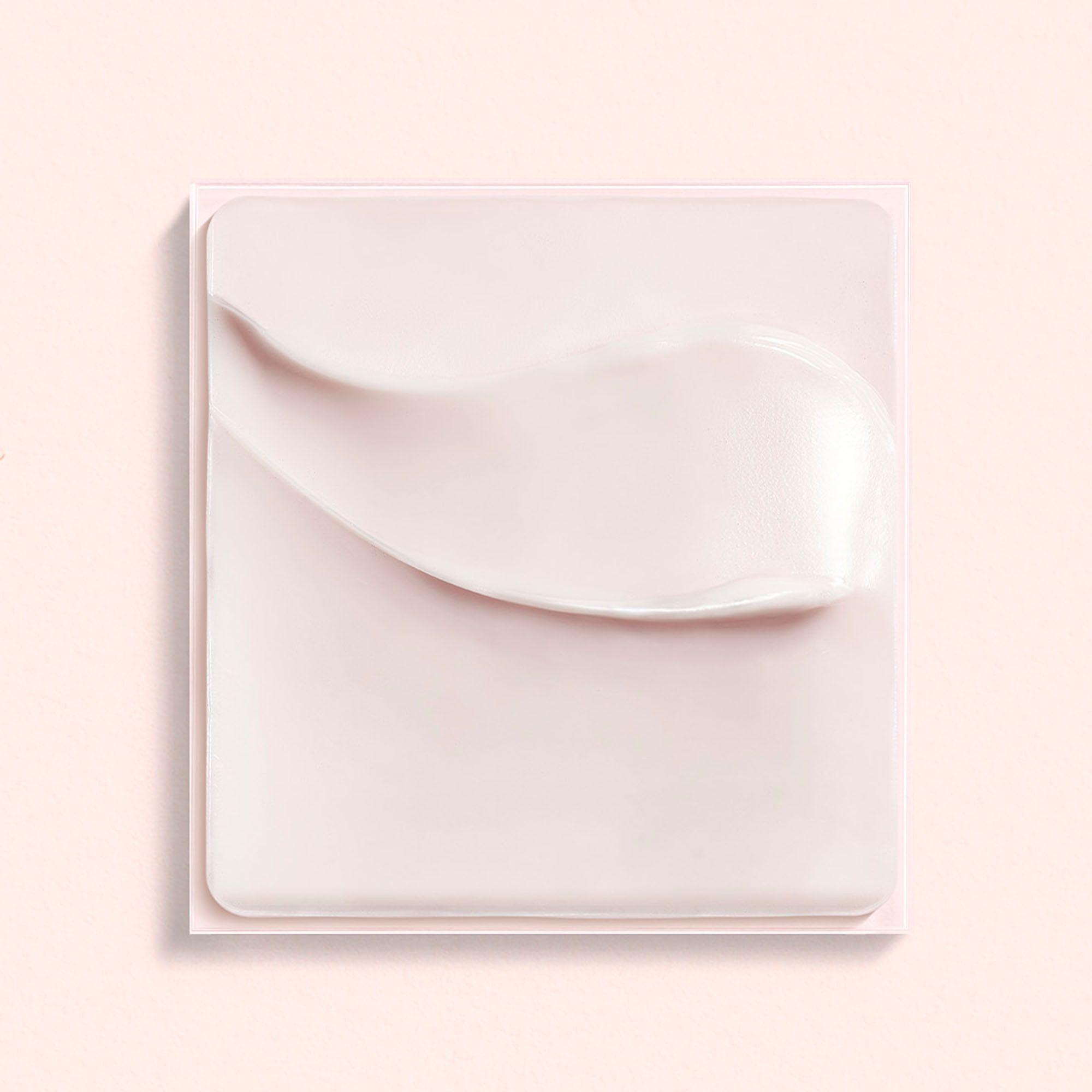 Crème-uitstrijk op vierkante ondergrond. Roze tint. Crèmetextuur zichtbaar.