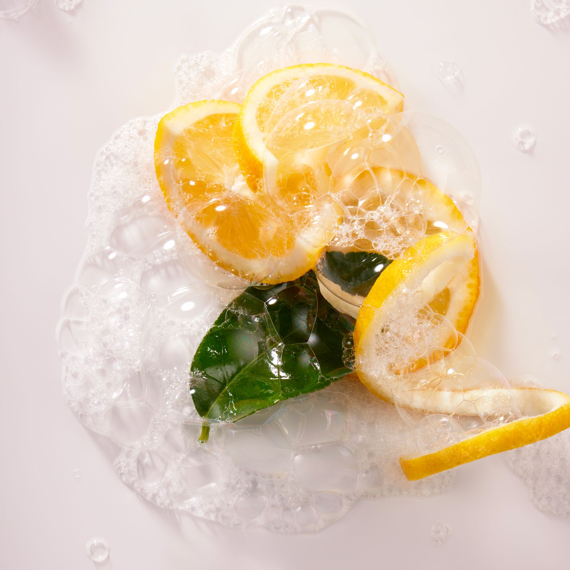 Gros plan sur des tranches de citron, des feuilles et des bulles de savon sur fond blanc.