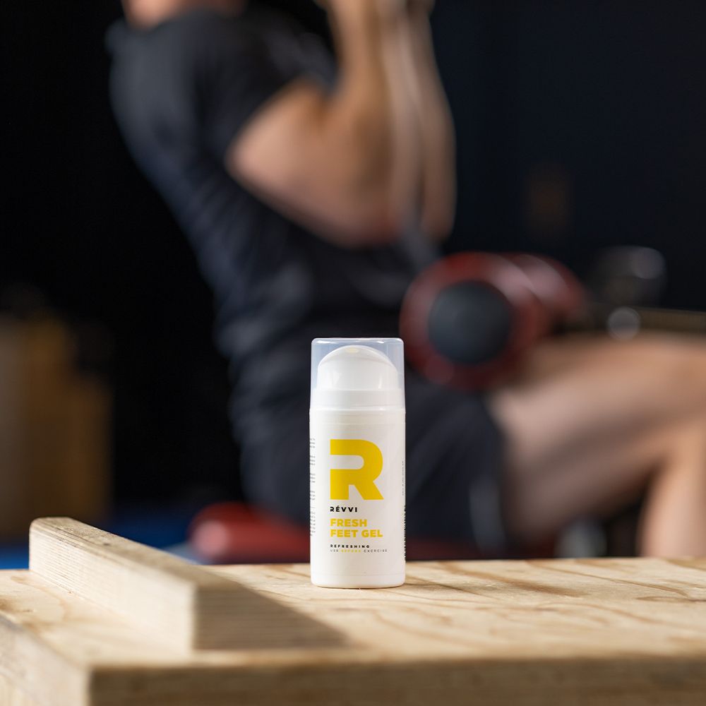 Kleine fles RÉVVI FRESH FEET GEL. Gele "R" en gele pomp. Op de achtergrond een persoon die traint.
