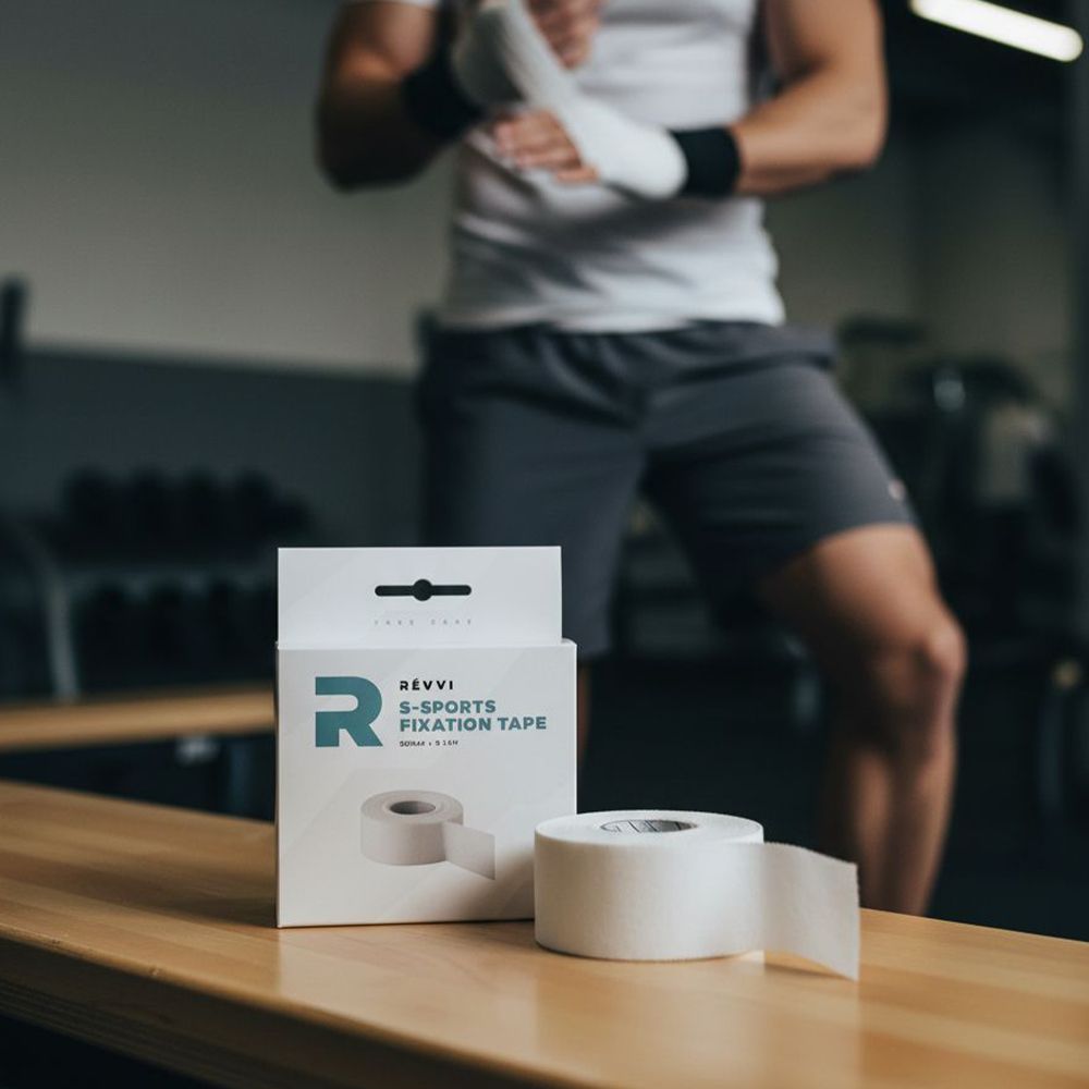 Een witte doos met Révvi S-Sports FIXATION TAPE en een rol tape op een houten bank. Een persoon op de achtergrond.