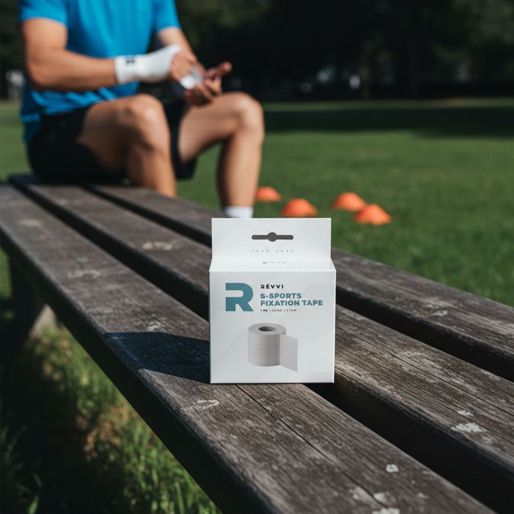 Verpakking RÉVVI S-Sports Fixation Tape op houten bank. Persoon op de achtergrond, tape om pols. Oranje kegels.