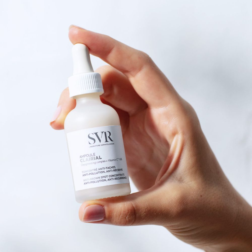 Hand houdt fles met pipet. Opschrift: SVR, Ampoule Clairial, Anti-Taches, Anti-Récidive.