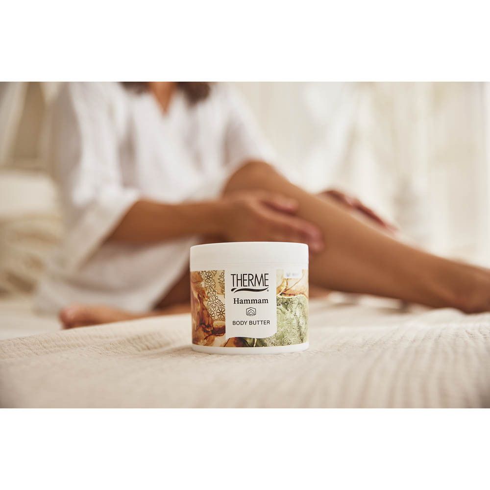 Persoon zit op een bed. THERME Hammam BODY BUTTER op het bed.