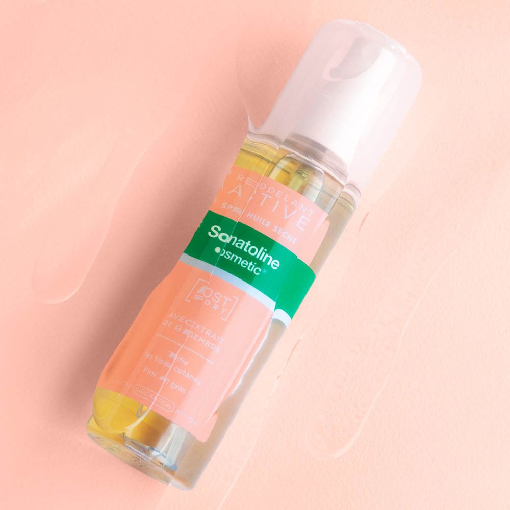 Flacon spray d'huile sèche. Vue de face. Verre transparent, liquide jaune, tête de pulvérisation blanche. Étiquette avec nom et marque.