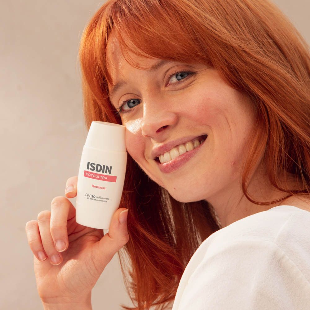 Vrouw houdt ISDIN FotoUltra Redness vast. Product op gezicht.
