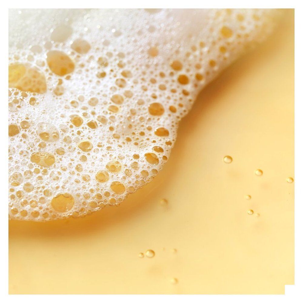 Close-up van schuim en gele vloeistof, Nuxe After-Sun Shampoo.