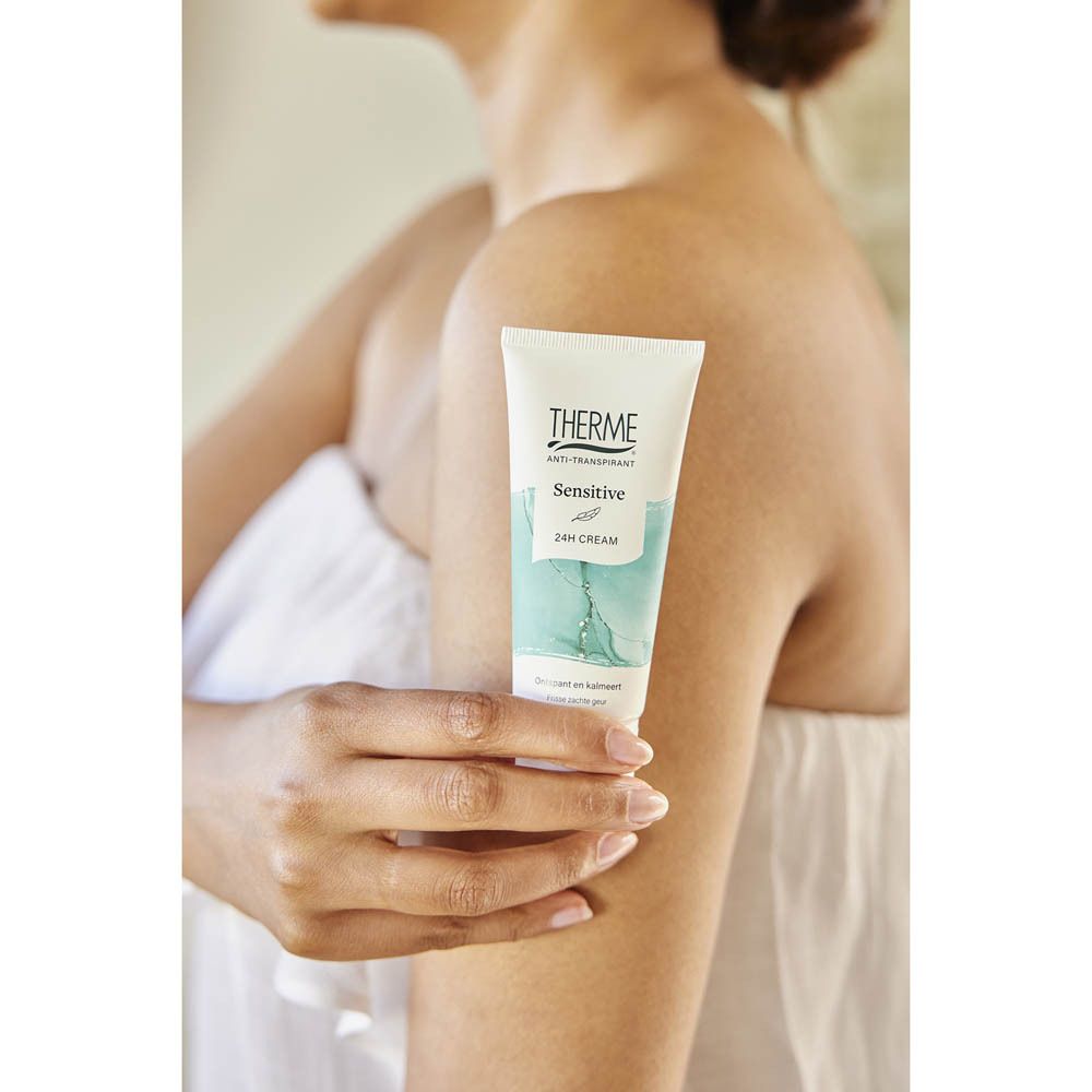 Une personne tient un tube de 24H Cream THERME Antitranspirant Sensitive à côté de son épaule.