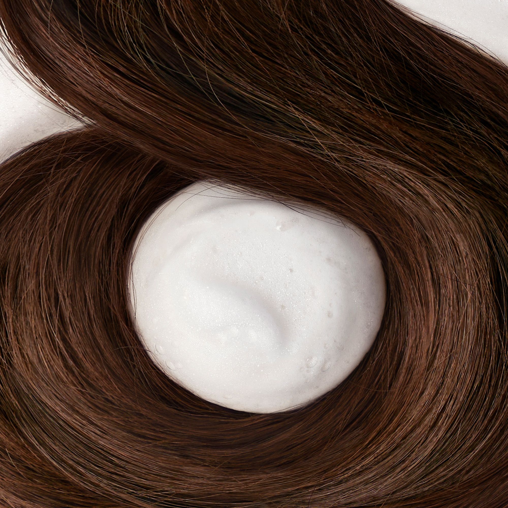 Wit schuim op bruin haar. Producttoepassing niet zichtbaar.