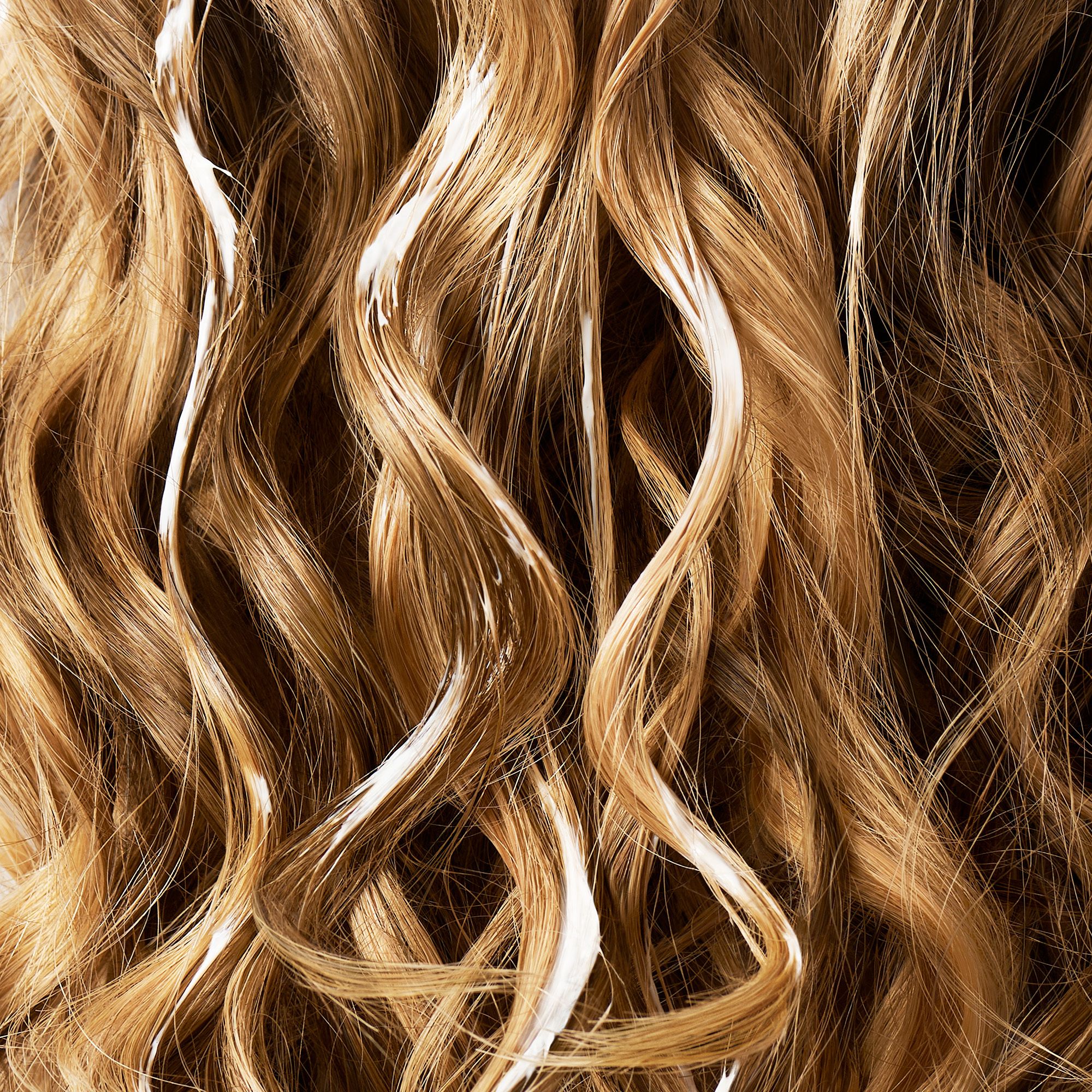 Haarlokken met witte substantie. Krullend, lichtbruin haar. De substantie lijkt te zijn aangebracht.