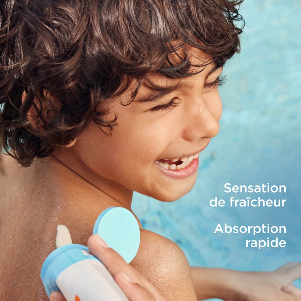 Enfant se fait appliquer ISDIN Fotoprotector Pediatrics Gel Cream Wet Skin. Eau bleue.