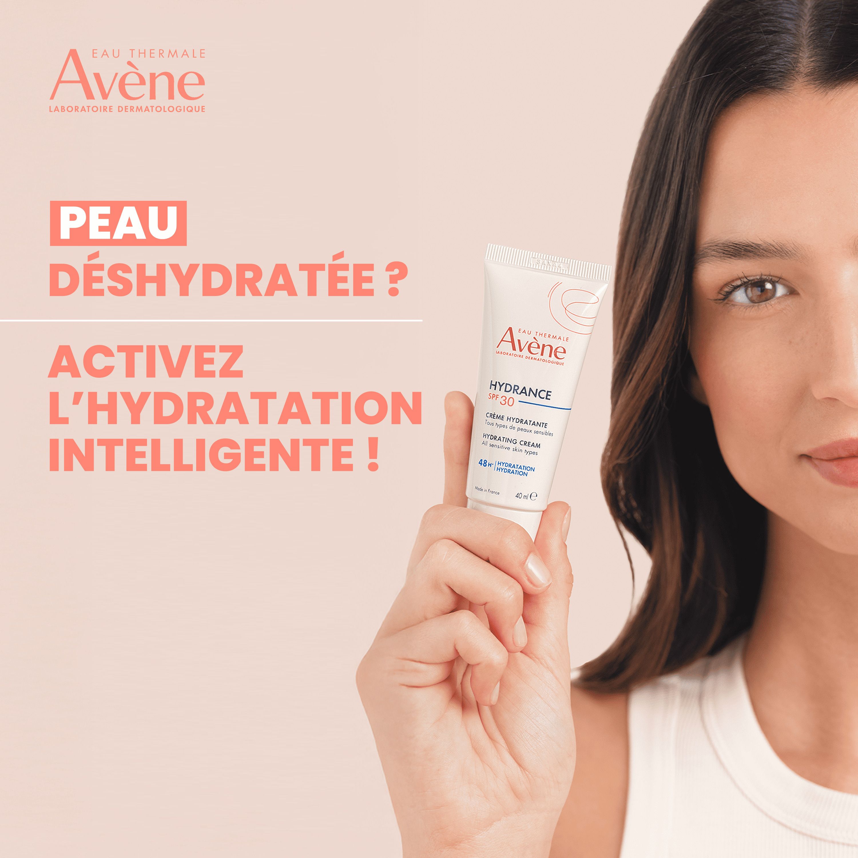 Femme avec produit. Tube blanc, marque Avène, Hydrance SPF 30. Texte: Peau déshydratée? Activez l'hydratation intelligente!