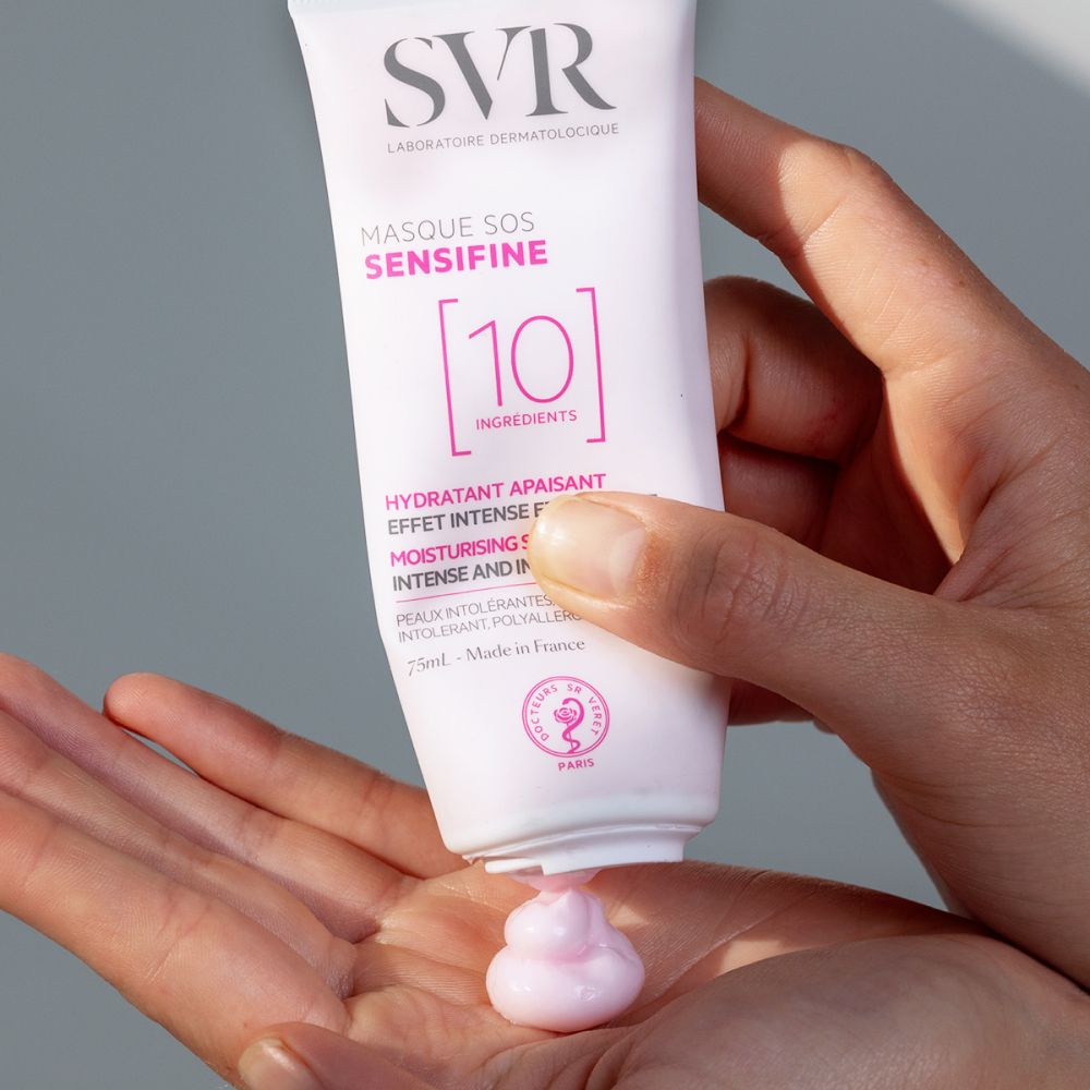 Mains tenant un tube. Crème rose sortant du tube. Inscriptions: SVR, Masque SOS Sensifine, 10 Ingredients.