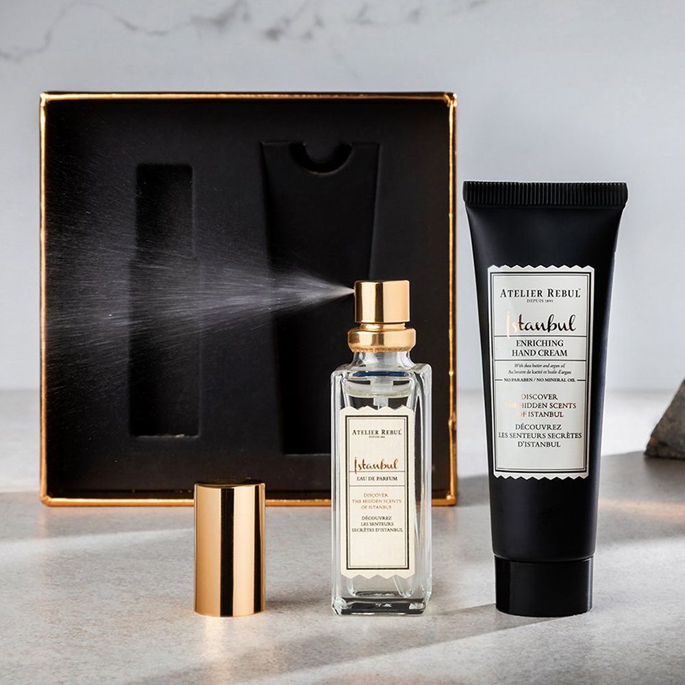 Flesje met gouden dop, spray. Handcrèmetube en zwarte geschenkdoos. Productnamen en merk zichtbaar.