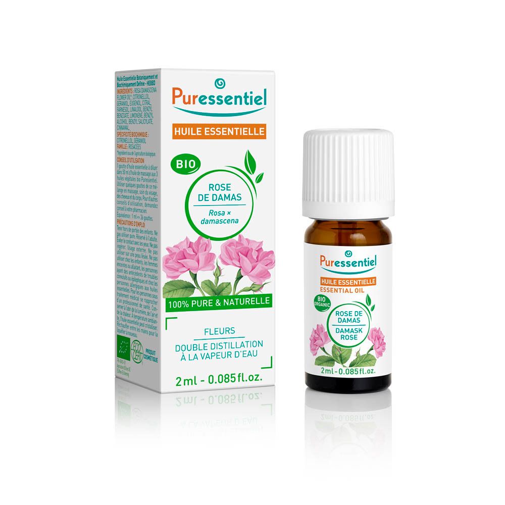 Petit flacon brun à bouchon blanc, contenant de l'huile essentielle de rose. À côté, une boîte en carton ouverte avec des images de roses.
