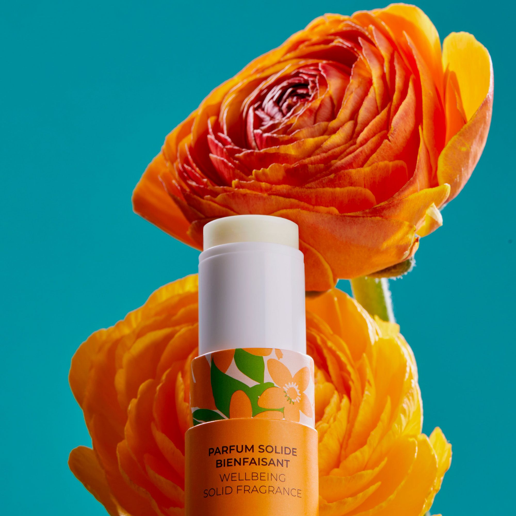 Produit dans son emballage ouvert, entouré de fleurs jaunes et fond turquoise.