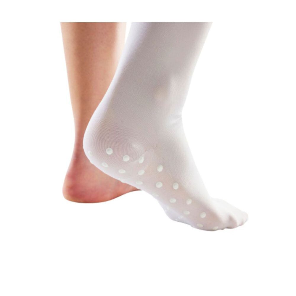 Chaussette blanche avec des points blancs sur la plante du pied. Un autre talon nu en arrière-plan.