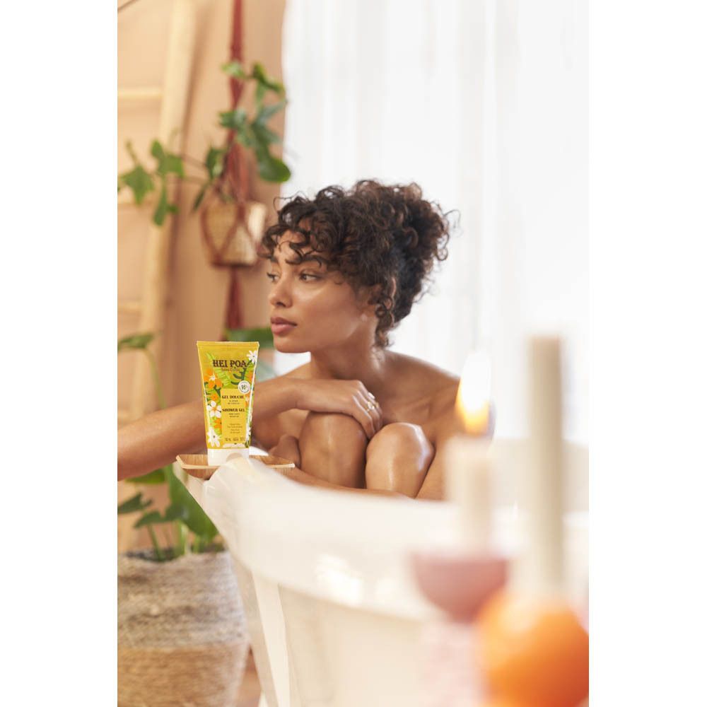 Femme dans une baignoire, tenant un tube de Gel Douche Monoi. Tube jaune sur un plateau. Scène de salle de bain.