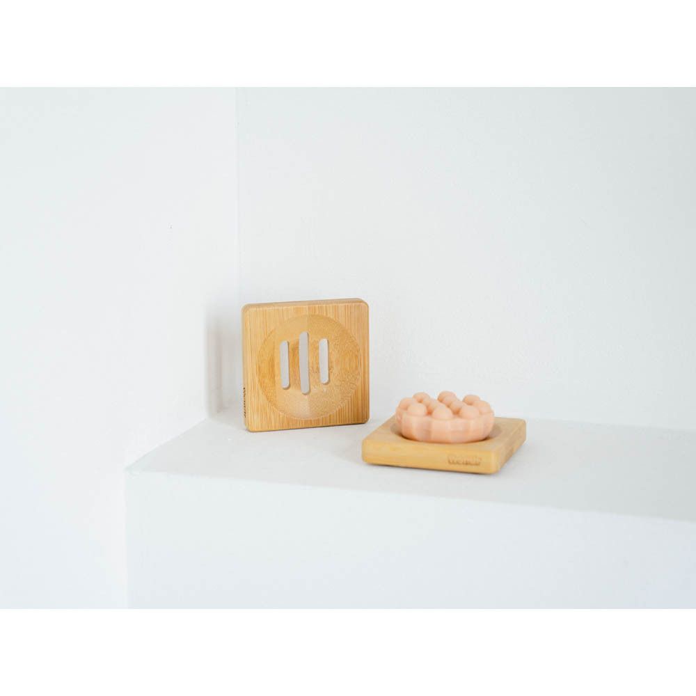 Deux porte-savons carrés en bambou. Un avec du savon. Sur une surface blanche.