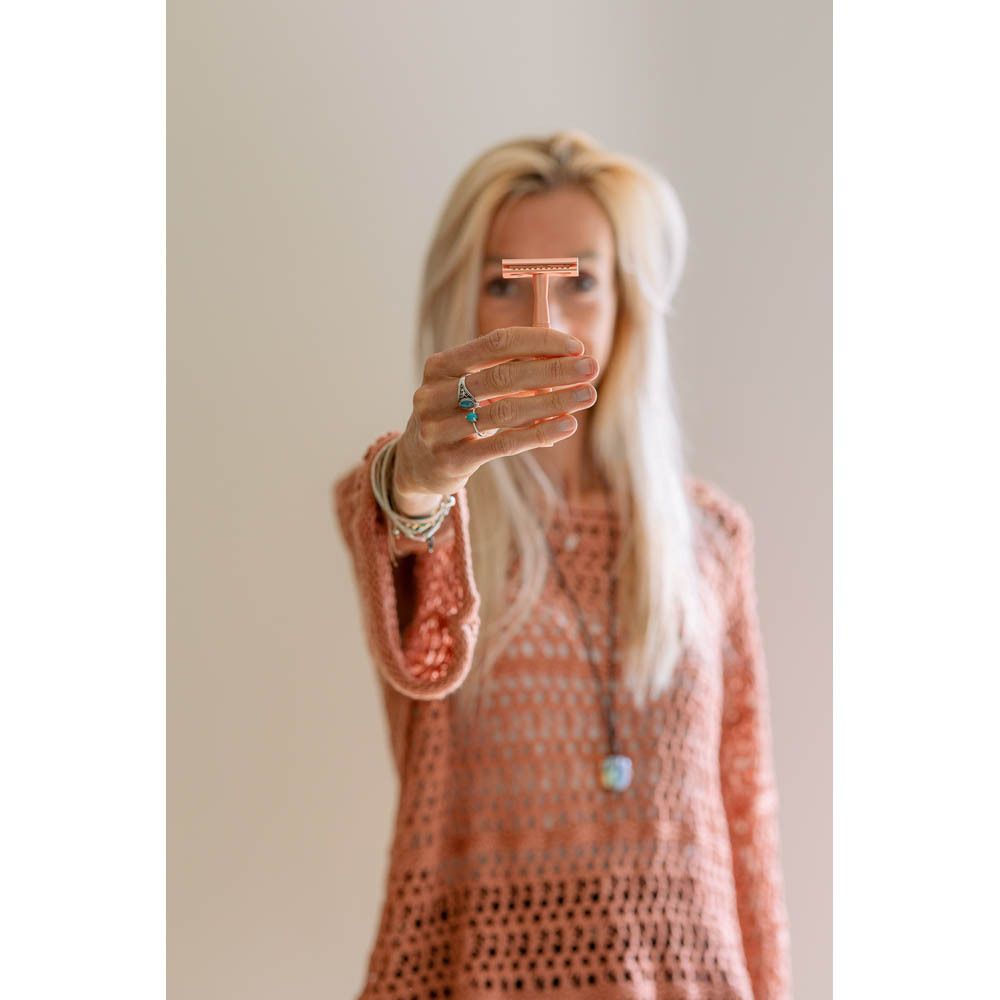 Vrouw houdt rosegouden scheermes voor zich. Ze glimlacht.