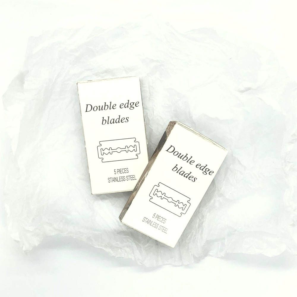 Twee kleine doosjes met scheermesjes op gekreukt papier. Opschrift: "Double edge blades".