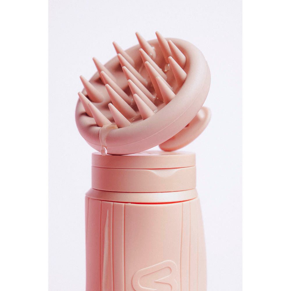 Roze siliconen hoofdhuidmassager op roze fles. Druppel op het apparaat.