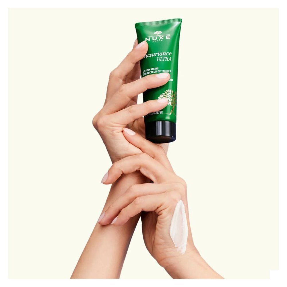 Handen die een tube NUXE Nuxuriance Ultra Handcrème vasthouden, een spoor crème op de rug van de hand.