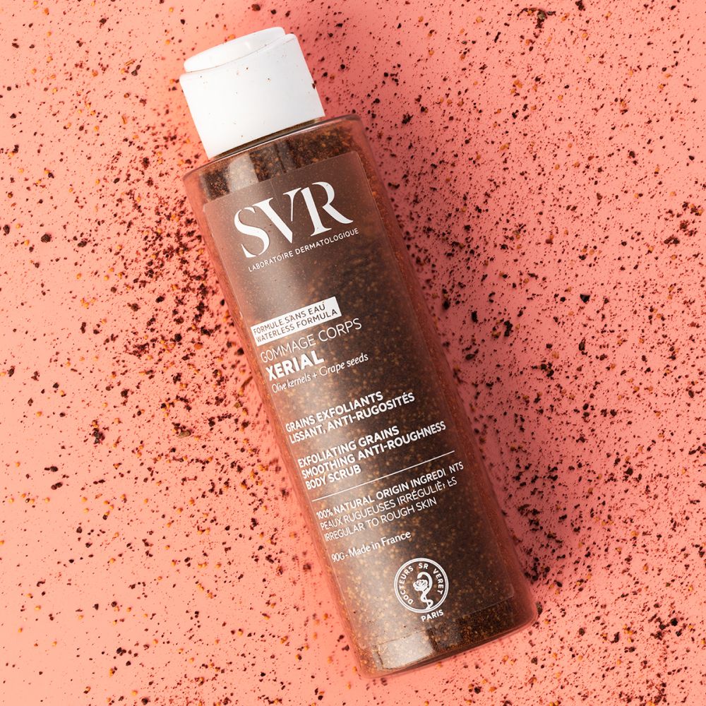 Lichaamsscrubfles op roze achtergrond. SVR-logo. XERIAL-tekst. Exfoliërende korrels.