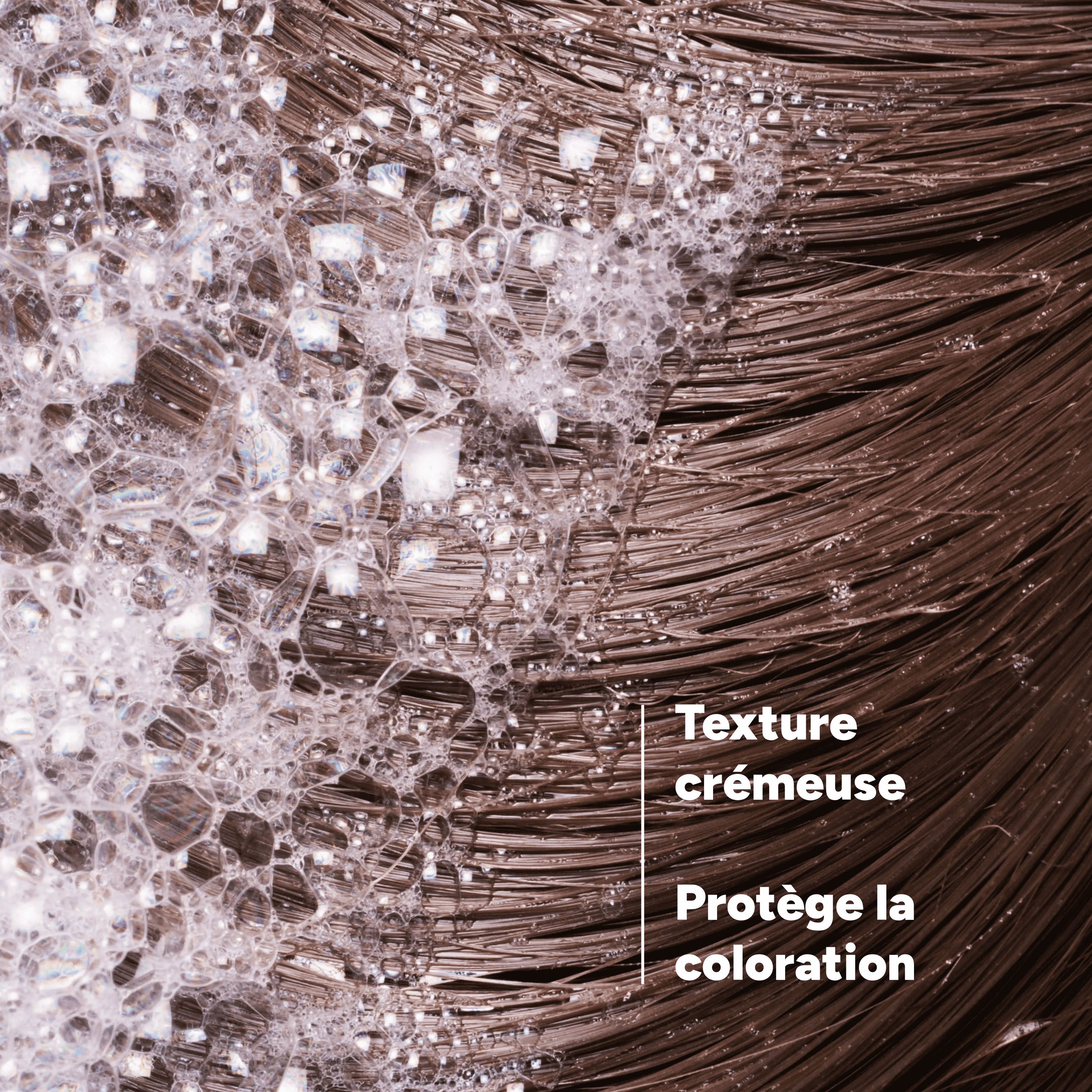 Gros plan sur cheveux bruns avec mousse. Texte: Texture crémeuse, protège la coloration.