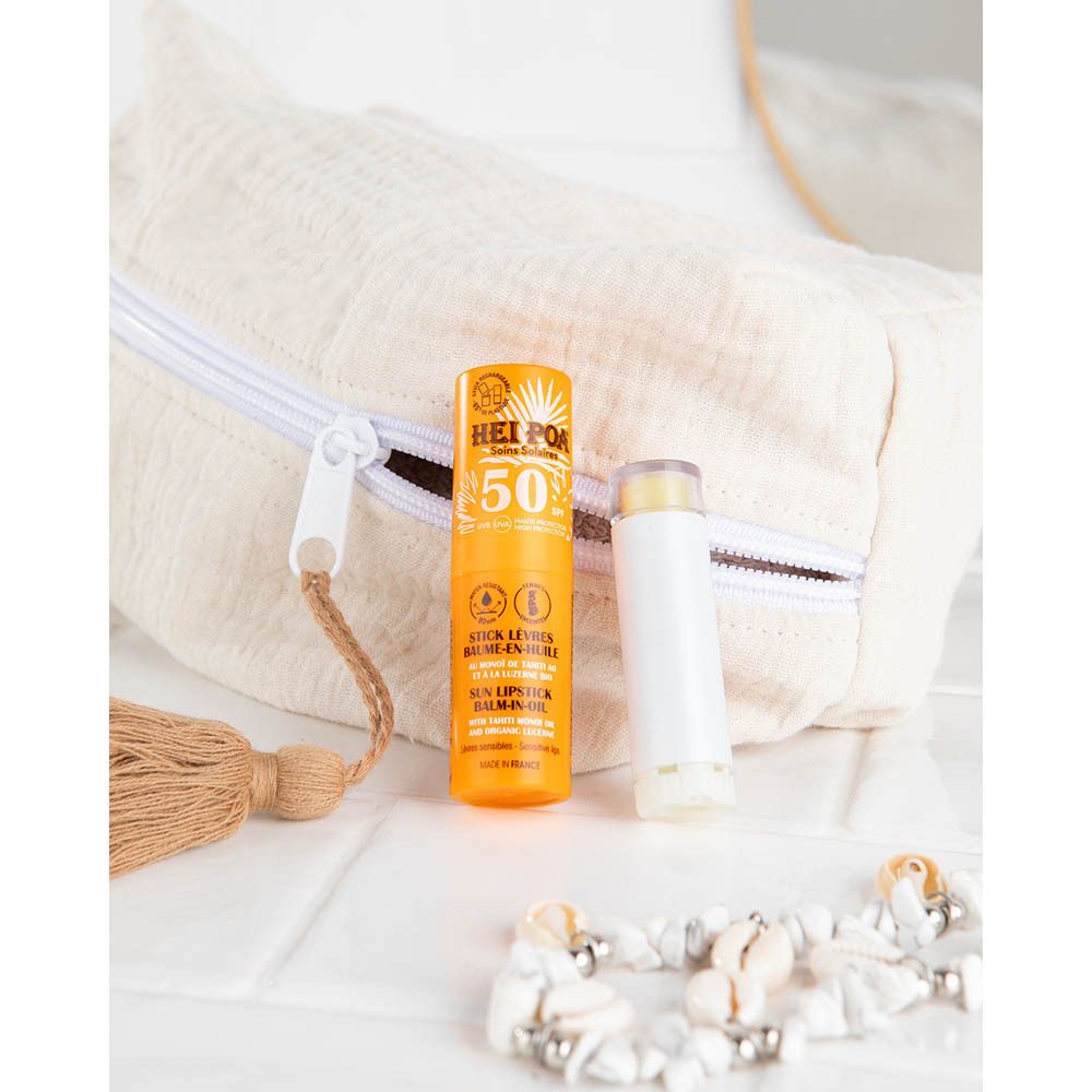 Lippenstift en open dop op een oppervlak. Tekst: Hei Poa, Soins Solaires, Stick Lèvres Baume-en-Huile, Sun Lipstick Balm-in-Oil.