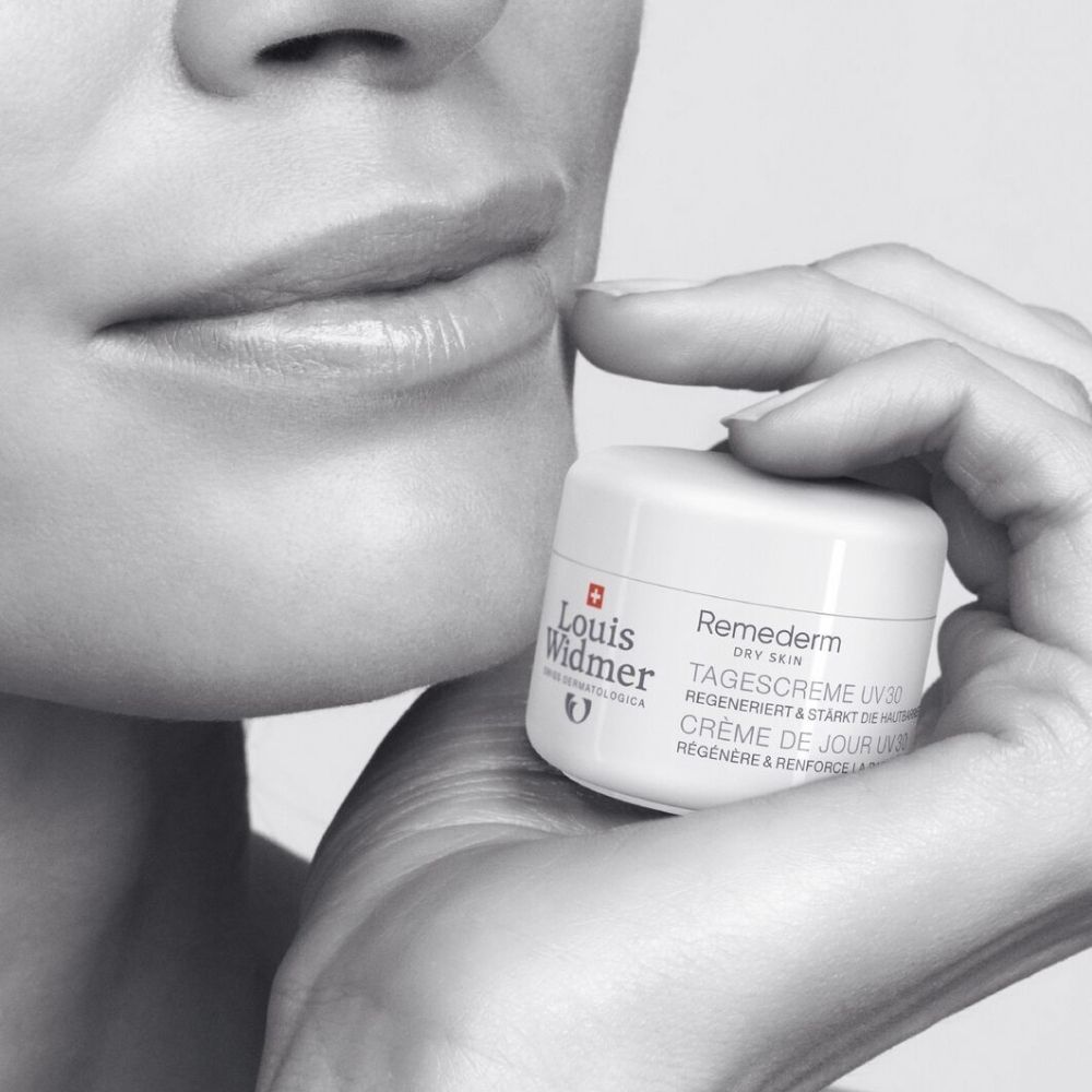 Persoon houdt een witte crème pot met Louis Widmer logo en productnaam Remederm Dagcrème UV30 vast.