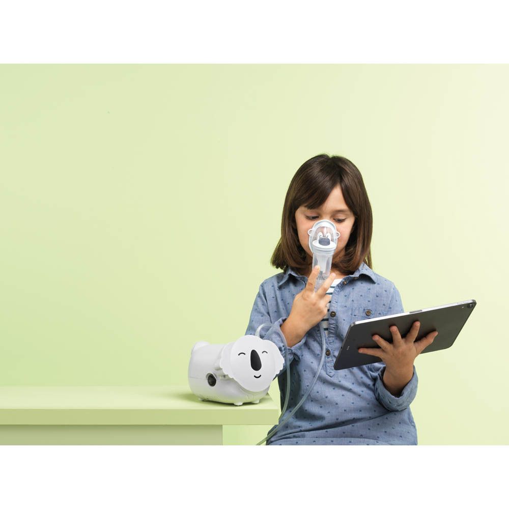 Kind houdt Koala vernevelaar vast. Tablet. Achtergrond: groene tafel, groene muur.