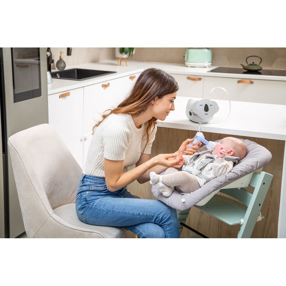 Femme et bébé. Bébé reçoit inhalation avec nébuliseur Koala. Fond : cuisine.