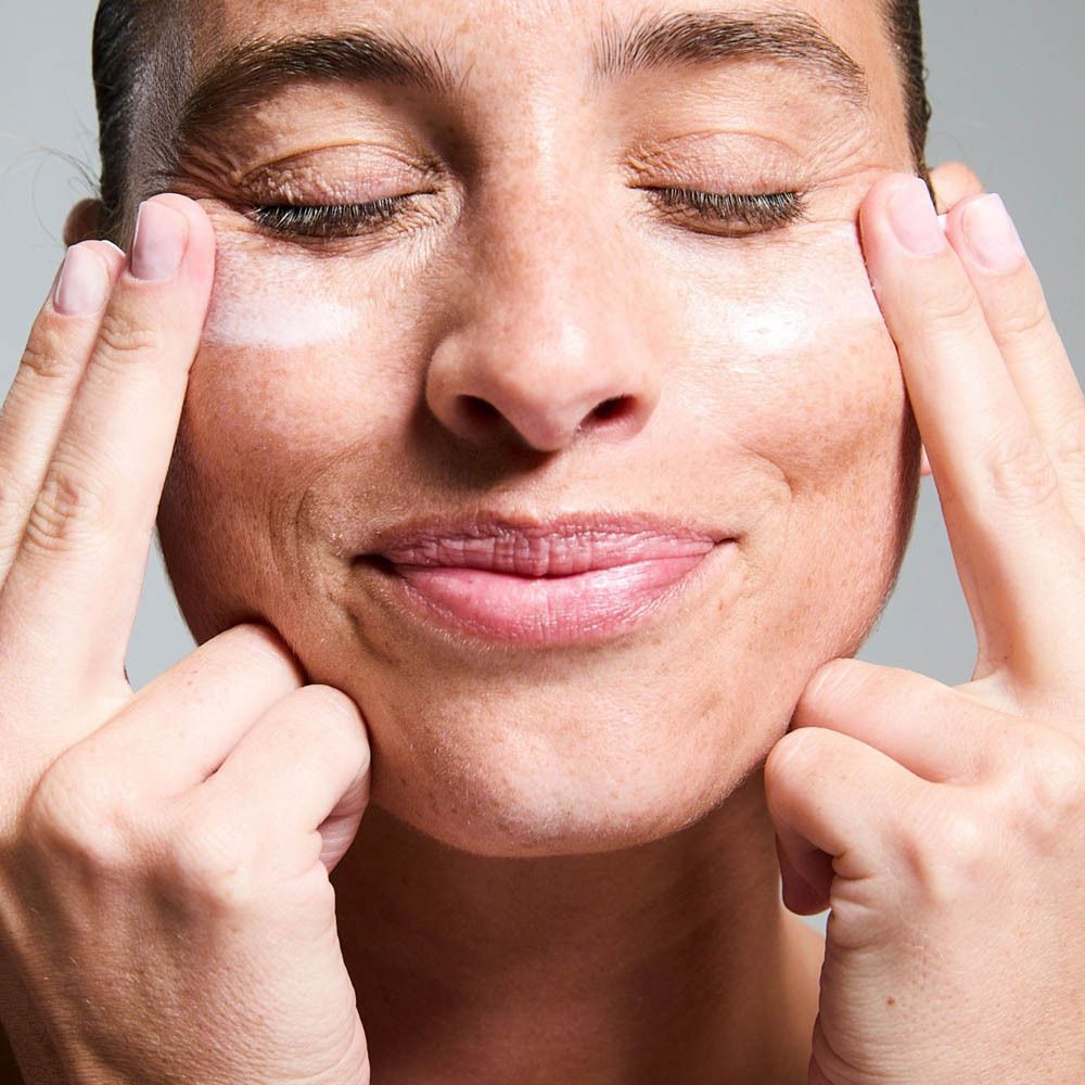 Gros plan d'une femme massant doucement le contour de ses yeux, les yeux fermés et un sourire aux lèvres.