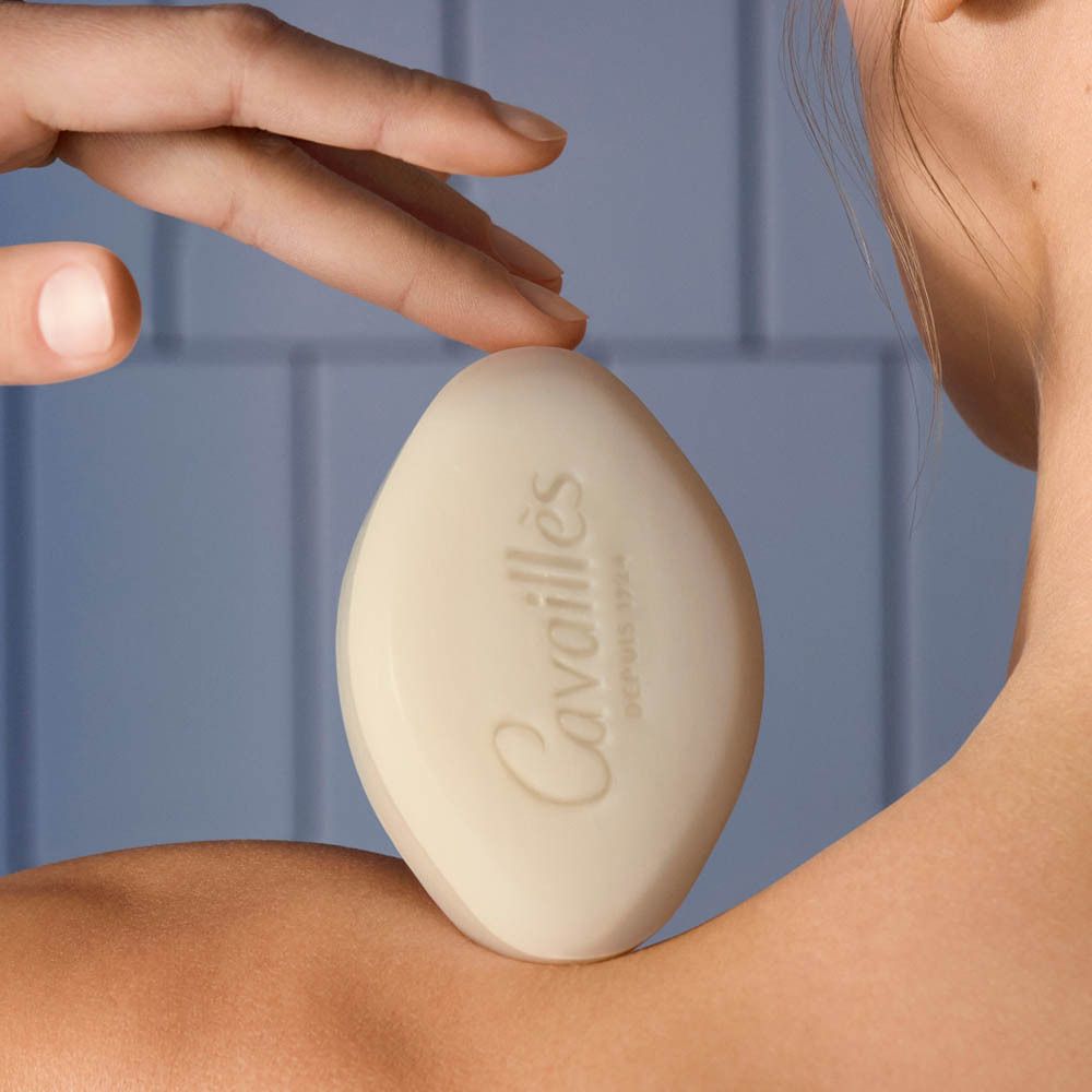 Savon beige ovale avec le nom Cavaillès. Une main touche le savon posé sur une épaule.