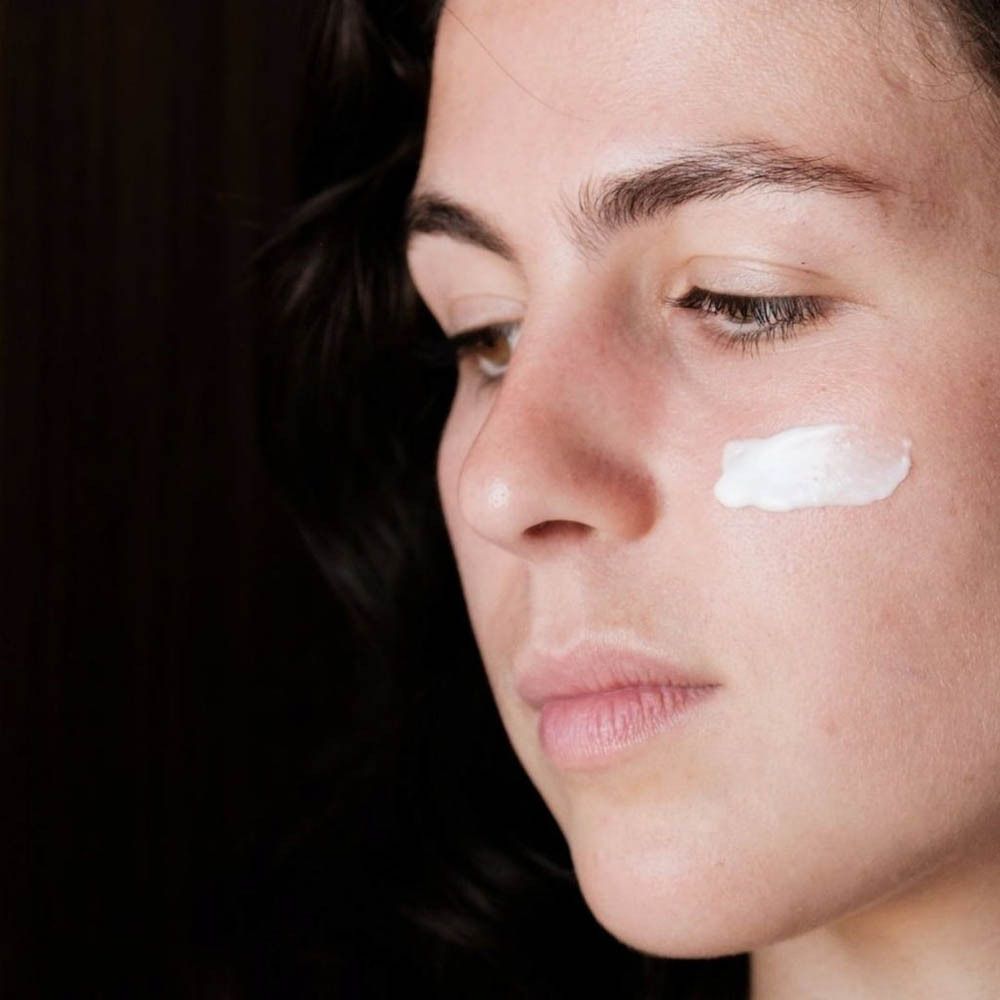 Vrouw met crème op de huid. Crème aangebracht op de wang. Donkere achtergrond.