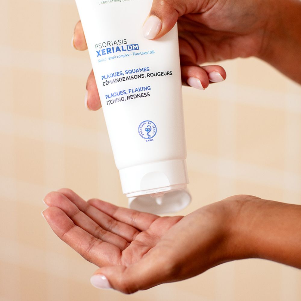 Persoon houdt tube SVR XERIAL DM vast. Tekst: Plaques, Squames, Démangeaisons, Rougeurs. Plaques, Flaking, Itching, Redness. Product wordt uitgeknepen.