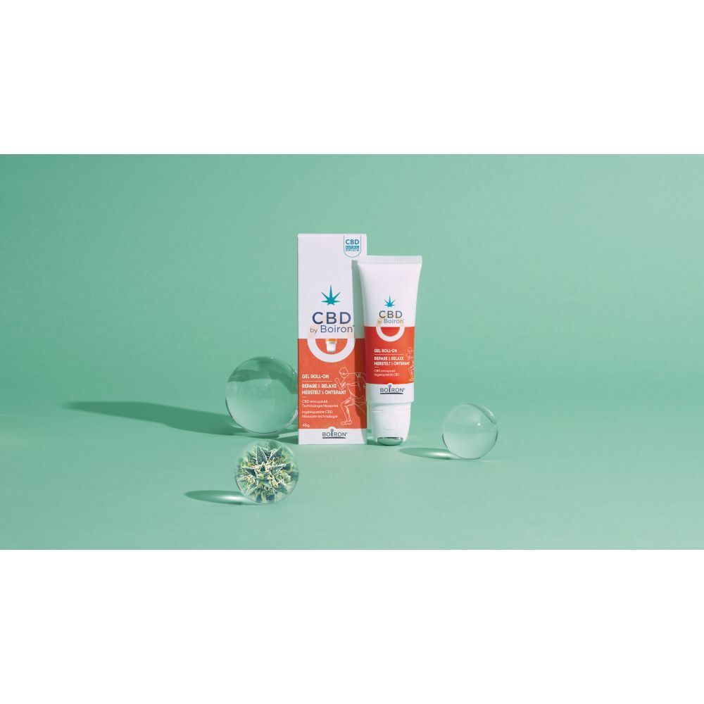 CBD by Boiron gel roll-on en verpakking op groene achtergrond. Glazen objecten op de achtergrond.