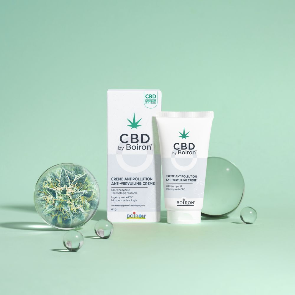 CBD by Boiron Crème Antipollution, tube et emballage. Fond avec boules de verre et décoration cannabis.