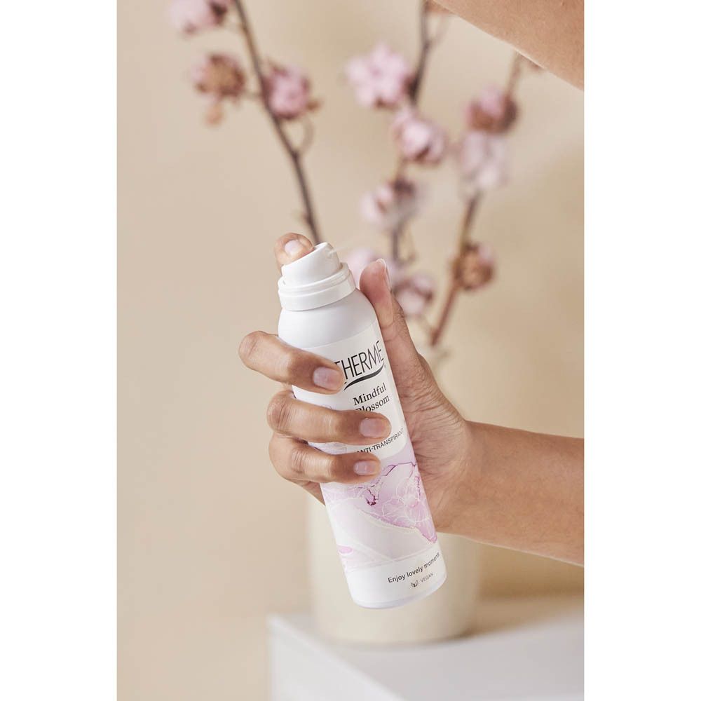 Hand houdt Therme Mindful Blossom spray vast. Achtergrond: bloemen. Product wordt vastgehouden.